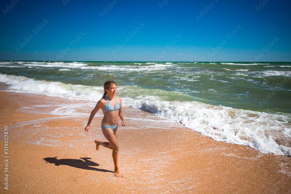 Joyful little active girl jumping on the waves of a stormy sea on a sunny warm summer day. Family Vacation Concept with Kids. Advertising space Joyful little active girl jumping on the waves of a stormy sea on a sunny warm summer day. Family Vacation Concept with Kids. Advertising space
