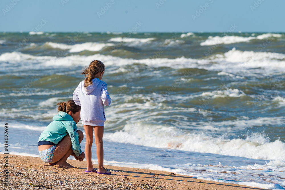 Rear view of little children playing on the beach on the sand near the stormy sea waves on a sunny summer day. Vacation concept with kids