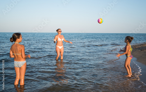 Pretty young woman plays ball with her charming daughters while swimming in the sea on a sunny warm summer day. Vacation concept with children. Advertising space