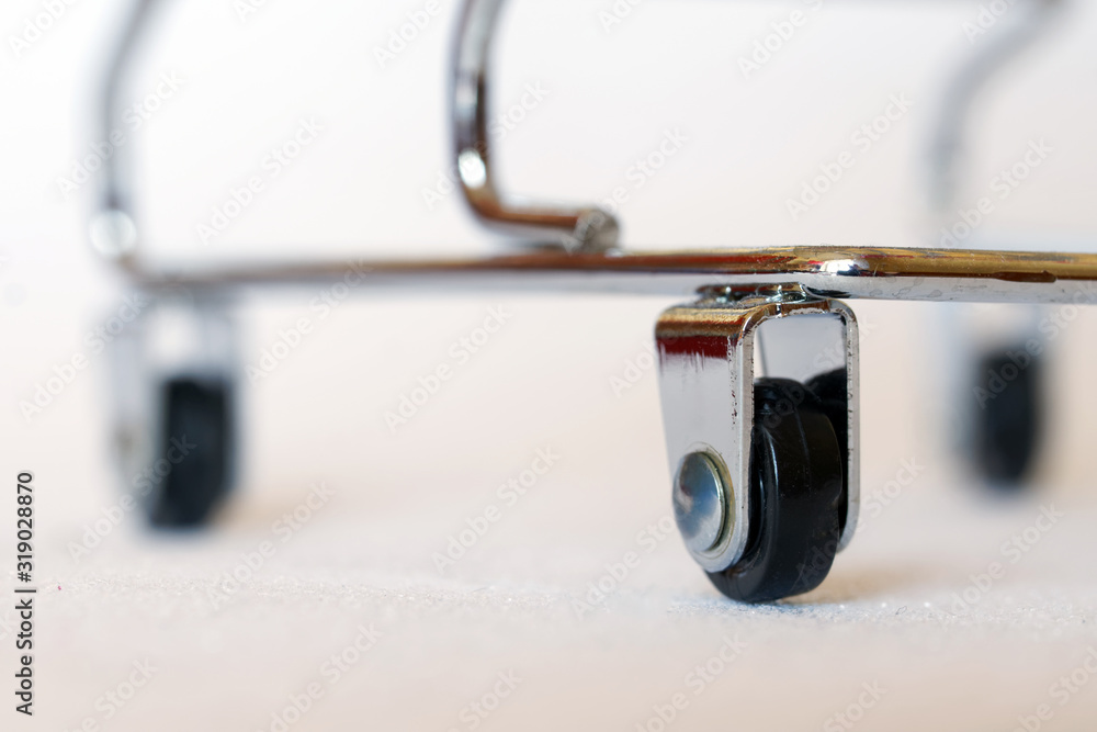 Wheels of a small metal trolley, similar to a trolley for transporting corpses in a morgue or a medical device. White background. Shallow depth of field Wheels of a small metal trolley, similar to a trolley for transporting corpses in a morgue or a medical device. White background. Shallow depth of field