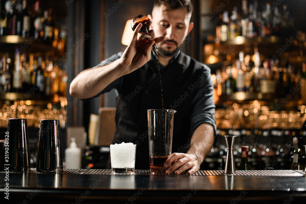 Male bartender pours cocktail with glass and vial