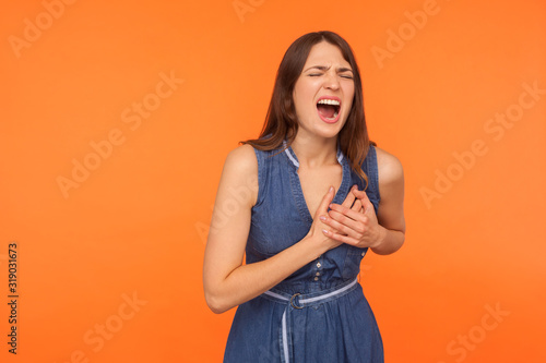 Acute pain in chest. Sick overworked brunette woman clutching breast and grimacing from painful cramp, heart attack at young age, cardiac disease. indoor studio shot isolated on orange background