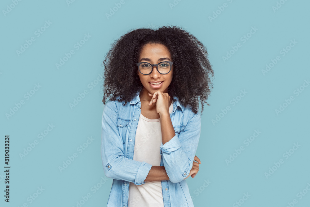 Freestyle. African girl in glasses standing isolated on gray touching chin curious Freestyle. African girl in glasses standing isolated on gray touching chin curious