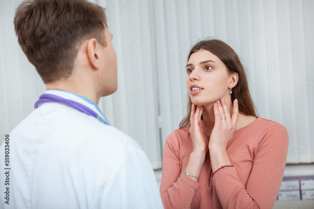Young woman with sore throat visiting doctor. Female patient with seasonal flu on medical appointment at the hospital Young woman with sore throat visiting doctor. Female patient with seasonal flu on medical appointment at the hospital