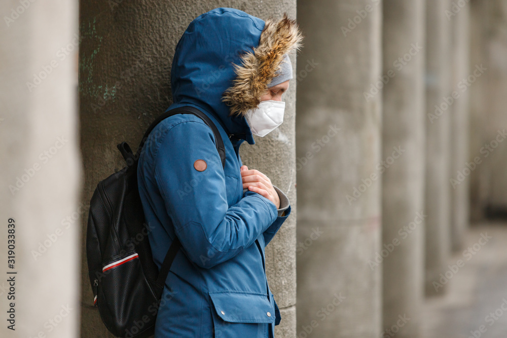 Unhealthy man with a hood holds hands on chest, wearing protective facial mask against transmissible infectious diseases and as protection against the flu or coronavirus in public places, outdoor. Unhealthy man with a hood holds hands on chest, wearing protective facial mask against transmissible infectious diseases and as protection against the flu or coronavirus in public places, outdoor.
