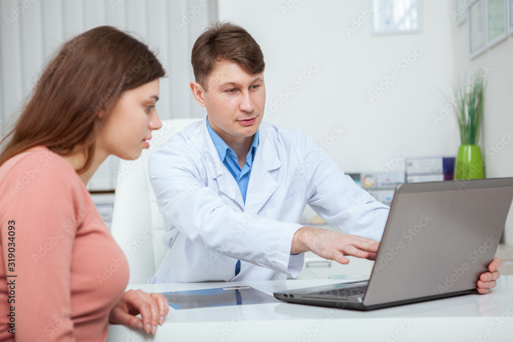 Mature male doctor showing something on laptop screen to his female patient during medical consultation Mature male doctor showing something on laptop screen to his female patient during medical consultation