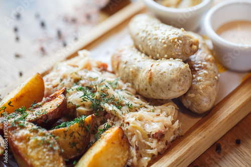 Lunch Time. Sausages potatoes and braised cabbage on board isolated on table close-up photo