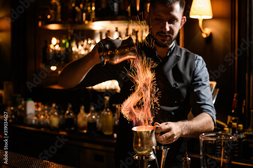 Male bartender flows burning liquid from mug to mug photo
