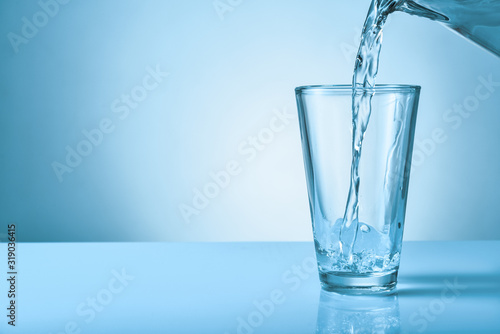 Pouring of fresh water into glass on color background