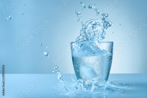 Glass of fresh water with splash on color background photo