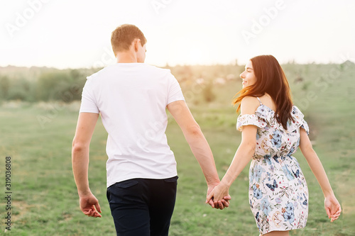 Young couple in love run on through grass field. Walking along grass field.