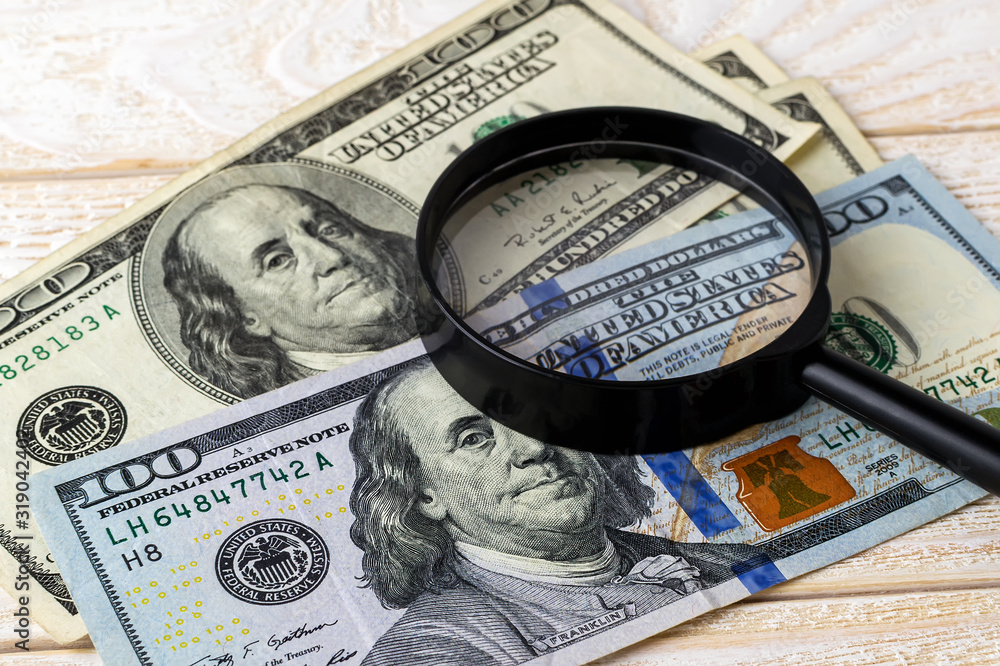 Magnifier on new and old dollar banknotes on a white wooden surface. Check the authenticity of money. Wealth, poverty and counterfeiting money concept. Magnifier on new and old dollar banknotes on a white wooden surface. Check the authenticity of money. Wealth, poverty and counterfeiting money concept.