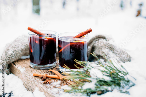 Mulled wine on a wooden board on a snowy table. Two glasses of hot wine with cinnamon and fresh vegetables..