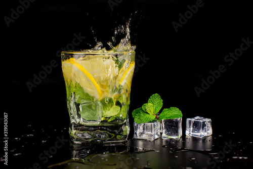  mojito cocktail drink with mint and lemon lime in a glass splash splashing out of a glass with ice cubes, drops and splashes on a black background