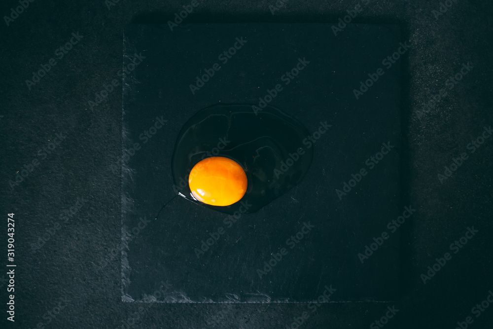 Broken egg on a slate plate on a black background view from voorhu Broken egg on a slate plate on a black background view from voorhu
