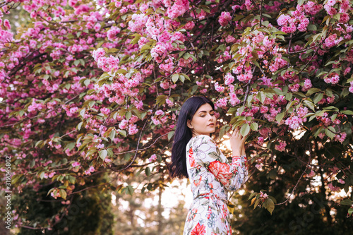 Fascinating tender woman standing next to pink blooming tree in garden