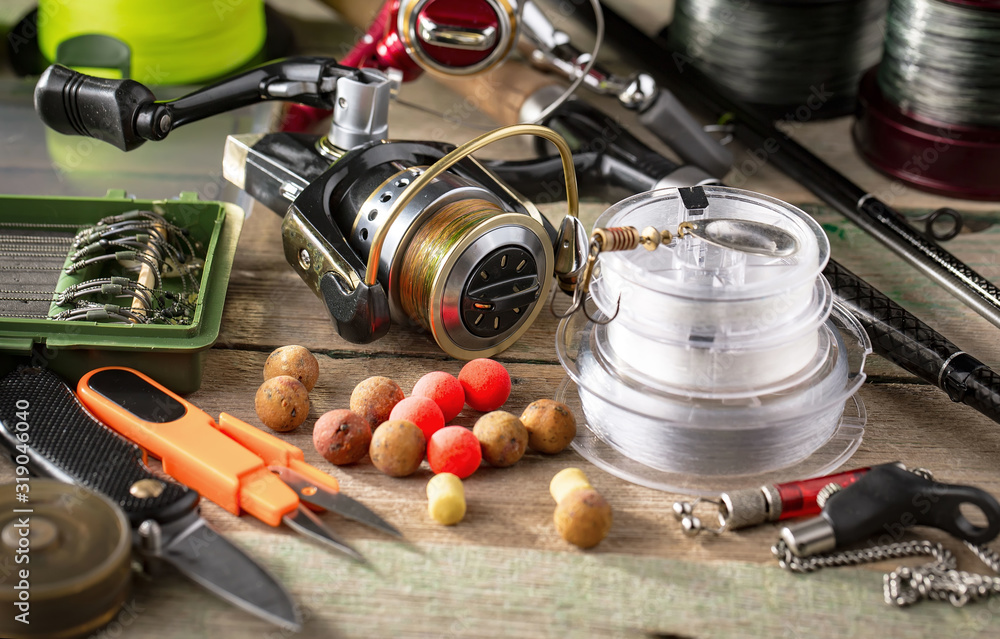 Fototapeta premium Fishing rods and spinnings in the composition with accessories for fishing on the old background on the table