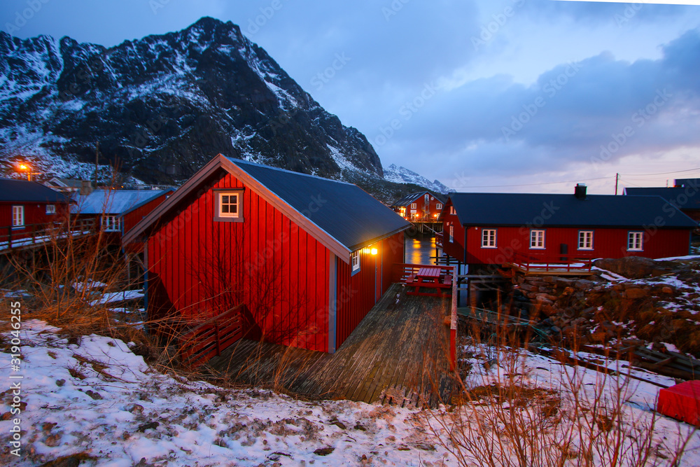 Small fishing village of A (Moskenes) at the end of the road of the Lofoten islands archipelago in northern Norway - Red rorbuer on stilts in winter at dawn in a fjord