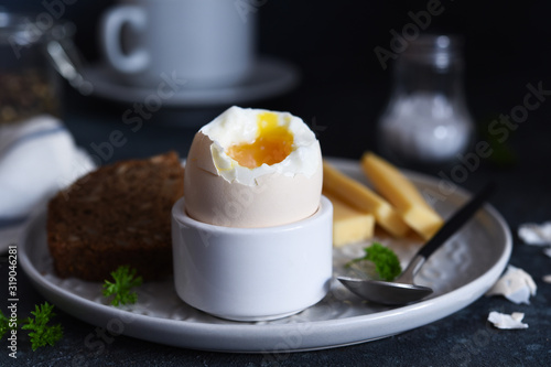 Classic breakfast - soft-boiled egg with whole grain bread on a dark background.