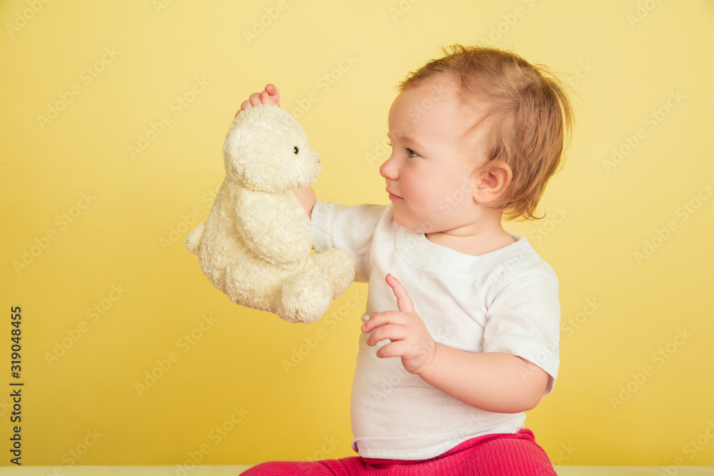 Caucasian little girl, children isolated on yellow studio background. Portrait of cute and adorable kid, baby playing with teddy bear. Concept of childhood, family, happiness, new life, education. Caucasian little girl, children isolated on yellow studio background. Portrait of cute and adorable kid, baby playing with teddy bear. Concept of childhood, family, happiness, new life, education.