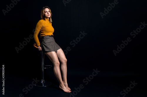 young cute girl sitting on a high chair against a dark background, copy space