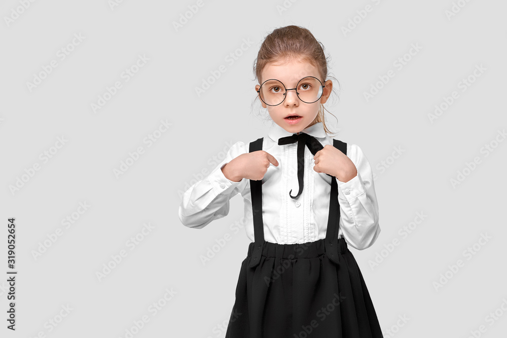 Amazed girl in a school uniform, round glasses show at herself. Studio shot. Isolated gray background. Amazed girl in a school uniform, round glasses show at herself. Studio shot. Isolated gray background.