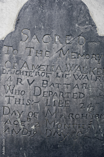 Large generic old solid stone gravestone with ancient lettering carved into it.