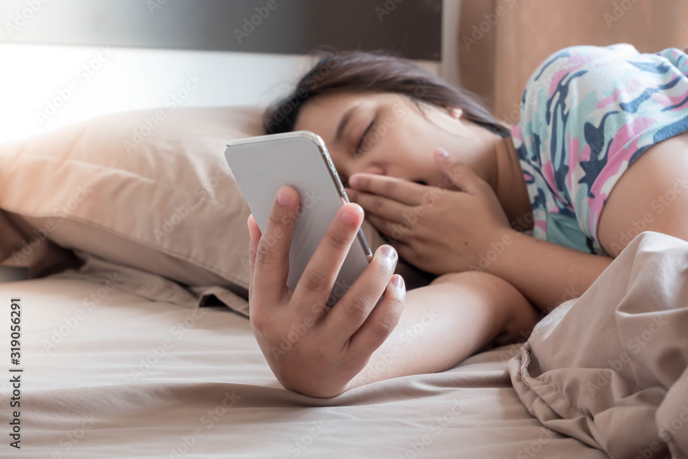 An Asian woman doesn't want to wake up in the morning after she hears the alarm clock from her mobile phone. An Asian woman doesn't want to wake up in the morning after she hears the alarm clock from her mobile phone.