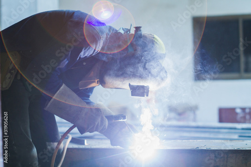 Welder cuts and joins metal using electricity (arc welding), in a welding mask and welders leathers protected,flare light background..