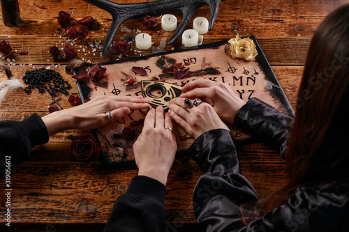 People conducting a seance using a Ouija Board, or Talking Spirit Board, with white candles. Shot from overhead.