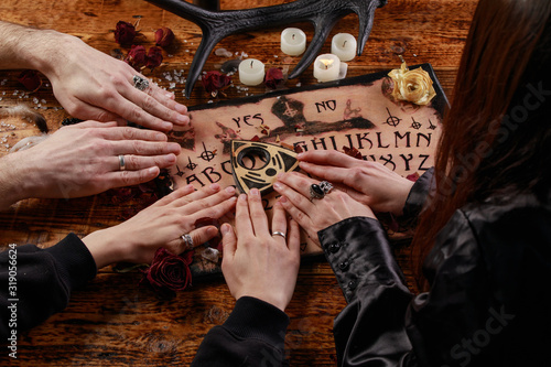 People conducting a seance using a Ouija Board, or Talking Spirit Board, with white candles. Shot from overhead.