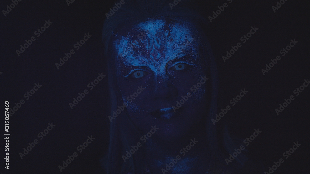Woman with a glowing blue face looks at the camera Woman with a glowing blue face looks at the camera