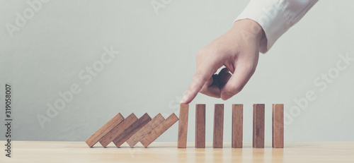 Hand stopping wooden domino business crisis effect or risk protection concept photo