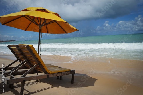 big yellow beach umbrella with chairs at a cloudy but still sunny beach