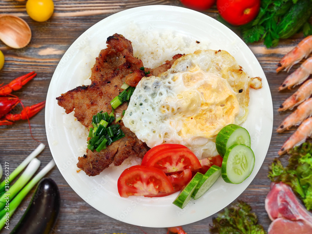 Com Tam - Closeup of vietnamese food: Delicious broken rice with egg pie and BBQ pork chop. fried egg meatloaf and pickles steak grilled pork ribs cucumber onion oil sweet chilies garlic fish sauce Com Tam - Closeup of vietnamese food: Delicious broken rice with egg pie and BBQ pork chop. fried egg meatloaf and pickles steak grilled pork ribs cucumber onion oil sweet chilies garlic fish sauce