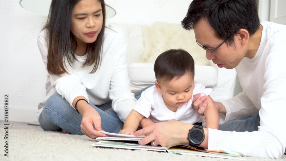 Happy modern Asian parents sitting on floor with cute infant boy and reading fairy tale while enjoying time together at home Happy modern Asian parents sitting on floor with cute infant boy and reading fairy tale while enjoying time together at home