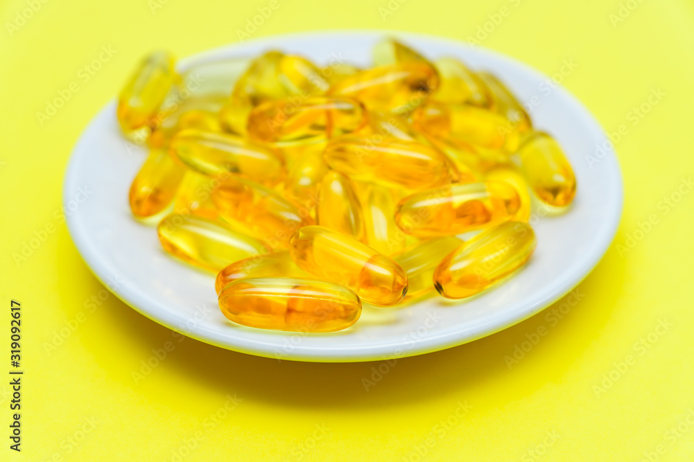 Cod liver oil omega 3 gel capsules on a plate on yellow background. Health care consept. close up Cod liver oil omega 3 gel capsules on a plate on yellow background. Health care consept. close up
