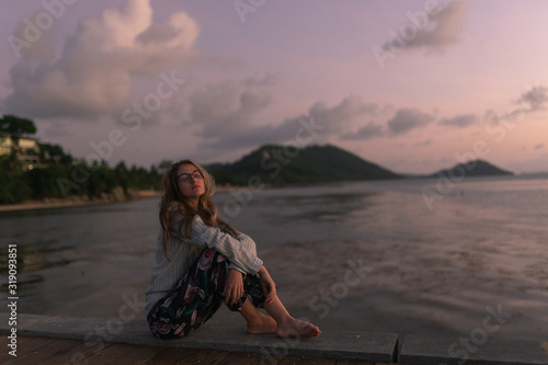 A beautiful girl with long hair stands and sits on a pier. Pensive and dreaming. Alone at sunset. Against the background of mountains and sea. Thailand, Samui © Underwater girls