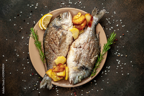Photography grilled dorado fish and fried potatoes on a plate with spices and lemon on a sto