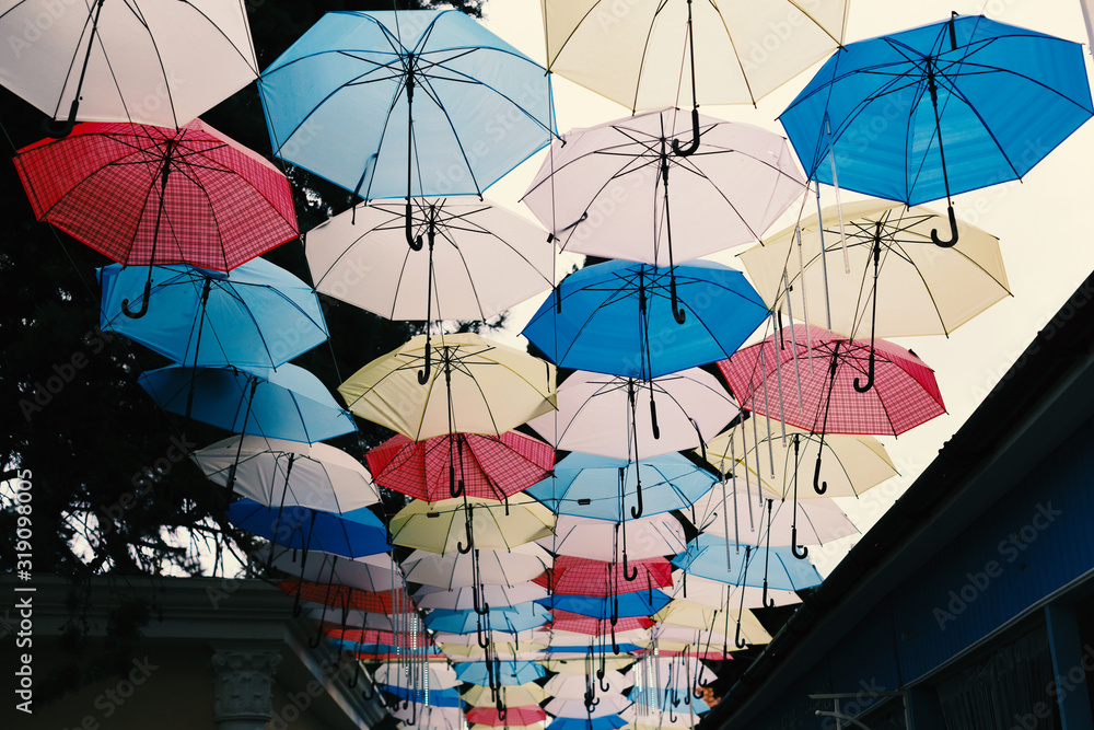 Many multi-colored umbrellas on a background of the cloudy sky.