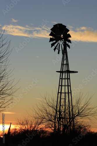 windmill at sunset with tree's and a fence in Kansas.