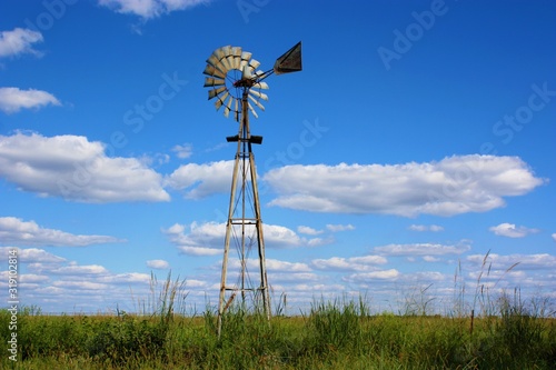 windmill in the field in Kansas west of Sterling Kansas with grass,blue sky, and white clouds.