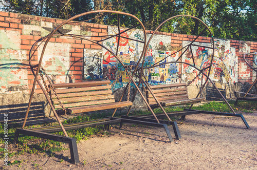 Old retro wooden bench swings in park near mosaic wall