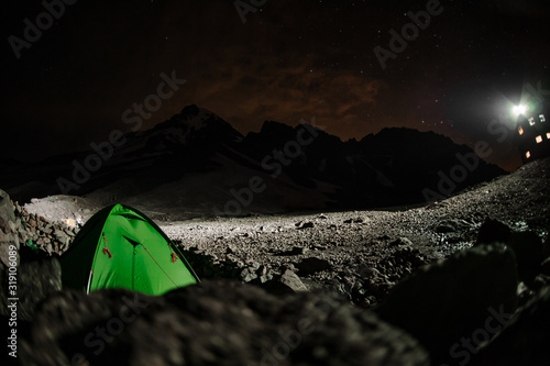 Landscape of the green tent standing on the mountain hill covered by rocks in the night