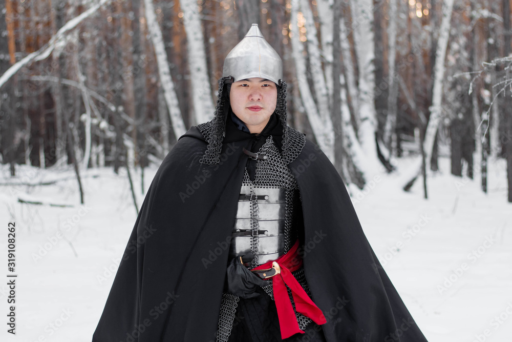 Portrait of a medieval warrior in armor, a helmet and a black cloak with a saber in his hands against the background of a winter forest an Portrait of a medieval warrior in armor, a helmet and a black cloak with a saber in his hands against the background of a winter forest an