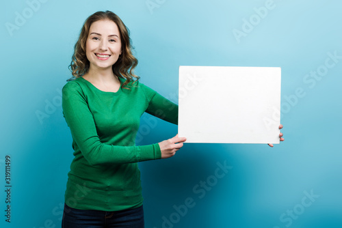 Smiling girl demonstrates white blank space for text on the side. Closeup, on blue background.