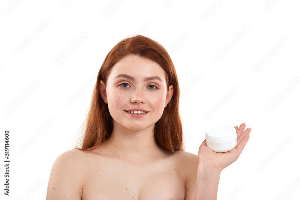 I love this cream. Young attractive red-haired girl with freckles demonstrating cosmetic product and looking at camera while standing in studio against white background I love this cream. Young attractive red-haired girl with freckles demonstrating cosmetic product and looking at camera while standing in studio against white background