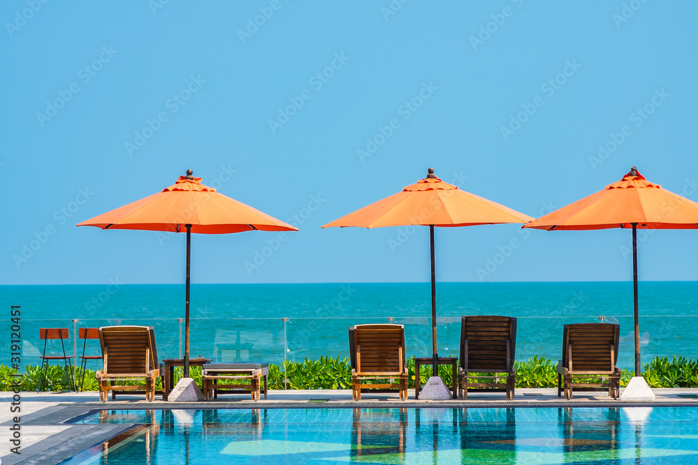 Umbrella and chair around outdoor swimming pool neary sea in hotel resort