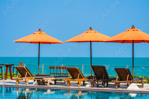 Umbrella and chair around outdoor swimming pool neary sea in hotel resort