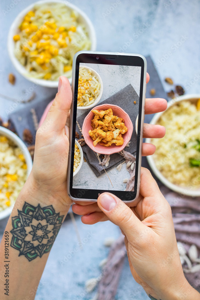 Woman take picture of vegan food with phone at her kitchen. Hand make a closeup smartphone photo of veggie lunch or dinner for blogging or social media content. Vegetarian healthy food.